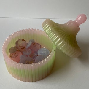 May include: A green and pink striped ceramic trinket box with a lid. The lid has a small knob on top. The box is filled with small buttons.
