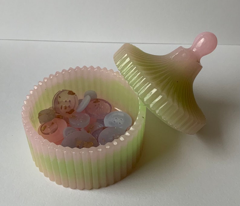 May include: A green and pink striped ceramic trinket box with a lid. The lid has a small knob on top. The box is filled with small buttons.