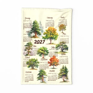 May include: A rectangular cream-colored fabric calendar for the year 2027. The design features twelve monthly grids, each accompanied by a watercolor-style illustration of a different tree species, including evergreens and deciduous trees.