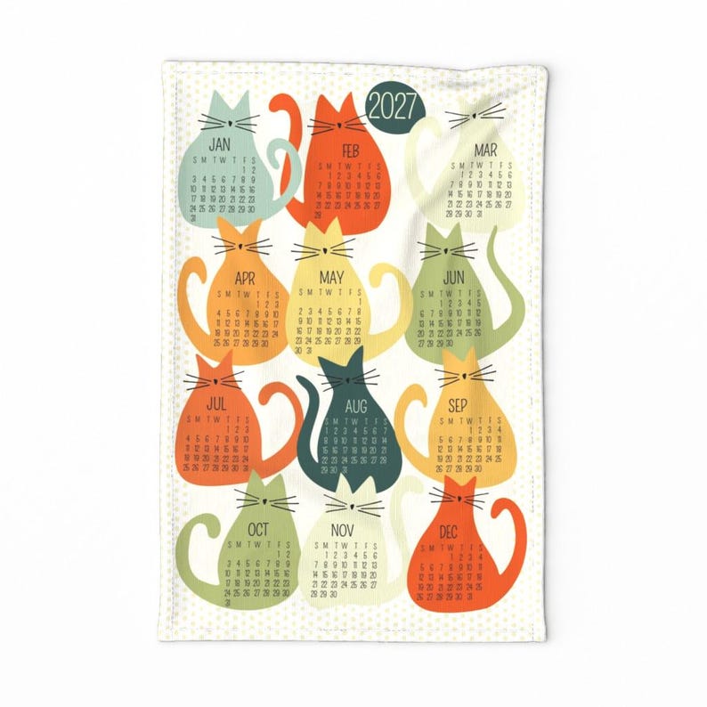 May include: A white rectangular tea towel featuring a 2027 calendar design. The calendar displays twelve colorful cat-shaped illustrations, each representing a month from January to December with its corresponding dates and days of the week.