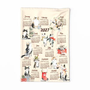 May include: A cream-colored tea towel featuring a 2027 calendar with watercolor illustrations of various cats for each month. The design includes handwritten month names, dates, and small festive cat drawings throughout the year.
