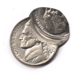 May include: A silver US nickel coin with a damaged edge. The coin features the profile of Thomas Jefferson on the obverse and the words "In God We Trust" and "Liberty" on the reverse.