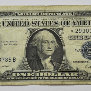May include: A vintage one dollar silver certificate featuring a portrait of George Washington. The certificate is dated 1957 and has the serial number 29303785 B.