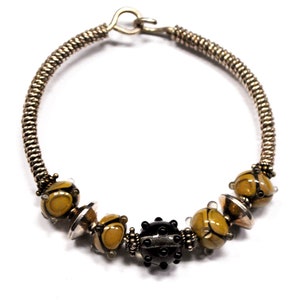 May include: A silver wire bracelet with a clasp and five glass beads. The beads are a mix of black and yellow.