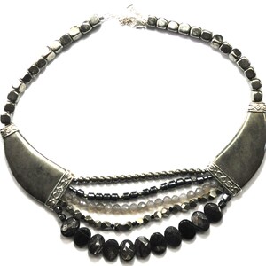 May include: A multi-strand necklace with a silver crescent moon pendant. The necklace features black, gray, and silver beads.
