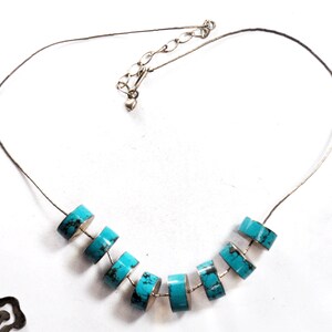 May include: A silver chain necklace with a heart charm and turquoise beads. The beads are round and have a slightly irregular shape.