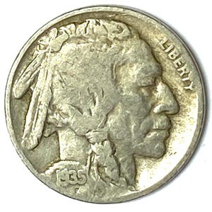 May include: A silver-toned Buffalo nickel coin featuring the profile of a Native American figure facing right, with the word LIBERTY printed along the upper right edge and the year 1935 stamped in the lower left quadrant of the circular coin.