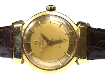 May include: A gold-tone Omega Seamaster wristwatch featuring a round gold dial with baton indices, gold hands, and a crown at the top. The watch is attached to a dark brown textured leather strap with visible stitching and gold-tone lugs.