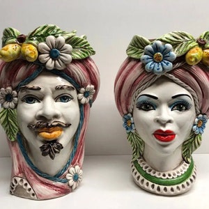 Puede incluir: Dos jarrones de cerámica con forma de cabeza con diseños florales y de hojas coloridos. Los jarrones están pintados en rosa, verde, azul, amarillo y blanco. Las caras están pintadas con rasgos realistas.