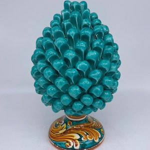 Puede incluir: Una escultura de piña de cerámica de color turquesa con una base detallada con un diseño floral y el texto "Le Ceramiche Siciliane  Antica  Arte".