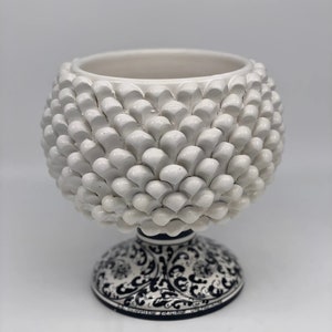 May include: White ceramic vase with a textured, pinecone-shaped design. The base of the vase is decorated with a black and white floral pattern.