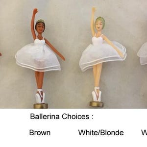 Op de afbeelding: Vier ballerina beeldjes met verschillende huidtinten en haarkleuren. Elk beeldje draagt een witte tutu en spitsschoenen. De tekst "Ballerina Choices" staat eronder, met de labels: Black, Brown, White/Blonde en White/Brunette.