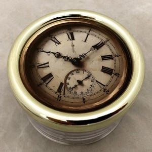 May include: A vintage pocket watch with a gold-colored bezel and a cream-colored face. The watch features black Roman numerals, delicate hands, and a smaller subdial. The watch is a classic timepiece.