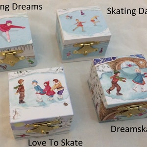Op de afbeelding: Vier kleine houten dozen met winterschaatsscènes. Elke doos heeft een andere illustratie op het deksel, met kinderen die schaatsen. De dozen hebben messingkleurige sluitingen en de tekst "Skating Dreams", "Skating Day", "Love To Skate" en "Dreamskater".