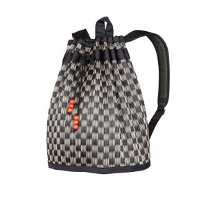 May include: A black and beige checkered drawstring backpack with a single black padded shoulder strap. The bag has a black drawstring closure and is decorated with three small orange beads.