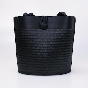 May include: A black tote bag with a woven texture and a black fabric top. The bag has two black fabric handles.