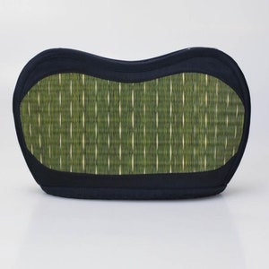May include: A black and green cushion with a woven pattern. The cushion has a curved shape and a black border. The center features a green and white woven design, creating a textured appearance. The cushion is designed for comfort and support.