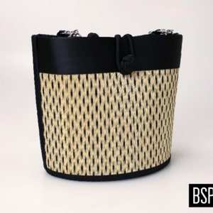 May include: A black and beige woven tote bag with black fabric trim and a black fabric handle. The bag has a woven pattern and a knotted handle.