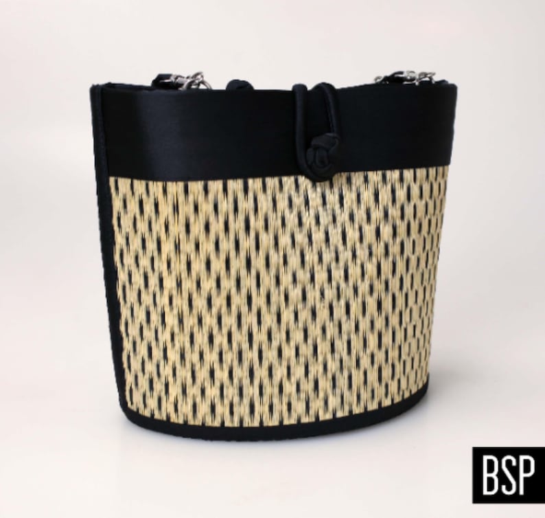 May include: A black and beige woven tote bag with black fabric trim and a black fabric handle. The bag has a woven pattern and a knotted handle.