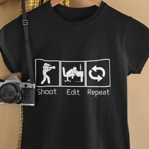 Könnte beinhalten: Schwarzes T-Shirt mit einer weißen Grafik aus drei Symbolen: eine Person, die ein Foto macht, eine Person, die an einem Computer bearbeitet, und ein Aktualisierungssymbol. Der Text unter den Symbolen lautet "Shoot Edit Repeat."