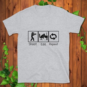 Könnte beinhalten: Graues T-Shirt mit einer Grafik aus drei Symbolen: einer Person, die ein Foto macht, einer Person, die an einem Computer bearbeitet, und einem Aktualisierungspfeil. Der Text unter den Symbolen lautet "Shoot Edit Repeat".