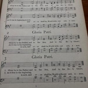 May include: A vintage sheet music page titled "Songs of Adoration" featuring musical notation and the text "Gloria Patri." The page is aged with visible wear and tear, and the text is in English.