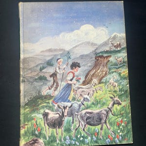 May include: Vintage hardcover book with a colorful illustration of a pastoral scene. The cover depicts two children, goats, and a mountain landscape. The artwork features a blue sky, green grass, and red and blue flowers. The book's edges show signs of wear.