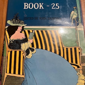 May include: The cover of a book titled "The Saturday Book - 25" with a blue background and the text "Edited by John Hadfield". The cover features a woman in a blue dress sitting on a striped couch, reading a book.