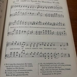 May include: Open book page with musical notation and lyrics. The text reads "O could we Speak the Matchless Worth." The page is aged with visible wear and tear, suggesting it is an antique or vintage item.