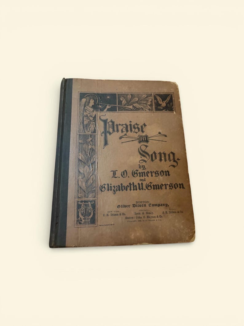 May include: An antique book titled "Praise in Song" by L.O. and Elizabeth U. Emerson. The cover is a faded brown with black decorative elements, including an angel playing a horn. The book is from the Silver, Ditson Company.