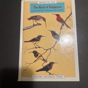 May include: A book cover with the title "The Birds of Singapore" by Clive Briffett & Sutari Bin Supari. The cover features an illustration of six colorful birds perched on branches.