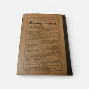 May include: An antique book titled "Sunday School" with a worn, tan cover and black spine. The cover features text including "Oliver Ditson Company" and book titles like "Praise in Song" and "Singing on the Way."