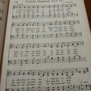 May include: Open book page with sheet music and the title "Faithful Shepherd, Feed me." The page is aged with visible musical notes and lyrics. The text includes phrases like "Hold me fast" and "I shall never stray."