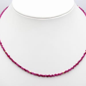 Può includere: Una collana di pietre preziose rosa con accenti dorati. La collana è composta da piccole perle rotonde e infilate su una catena sottile.