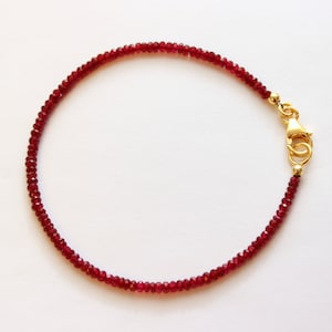 Könnte beinhalten: Ein zartes Armband aus roten Edelsteinen mit einem goldenen Verschluss. Das Armband besteht aus kleinen, runden Perlen und ist perfekt für den Alltag.