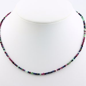 Può includere: Una collana delicata realizzata con piccole pietre preziose sfaccettate in tonalità rosa, blu e verde. La collana è infilata su una catena d'argento.