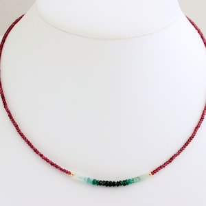 May include: A delicate necklace with small red and green gemstone beads. The necklace is made of gold and features a gradient of red, green, and light blue beads.
