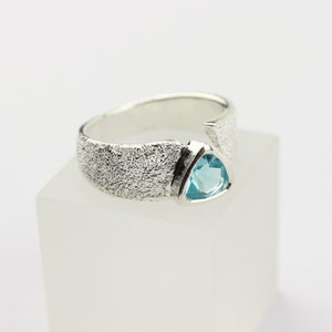 May include: A silver ring with a textured band and a light blue triangular gemstone.