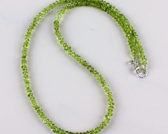 May include: A green peridot gemstone necklace with a silver clasp. The necklace is made of small, faceted beads.