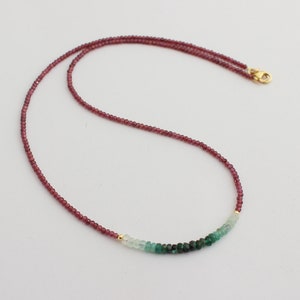 May include: A delicate gold chain necklace with a gradient of green and pink gemstones. The necklace features small, round beads in shades of pink, transitioning to light green and then dark green.