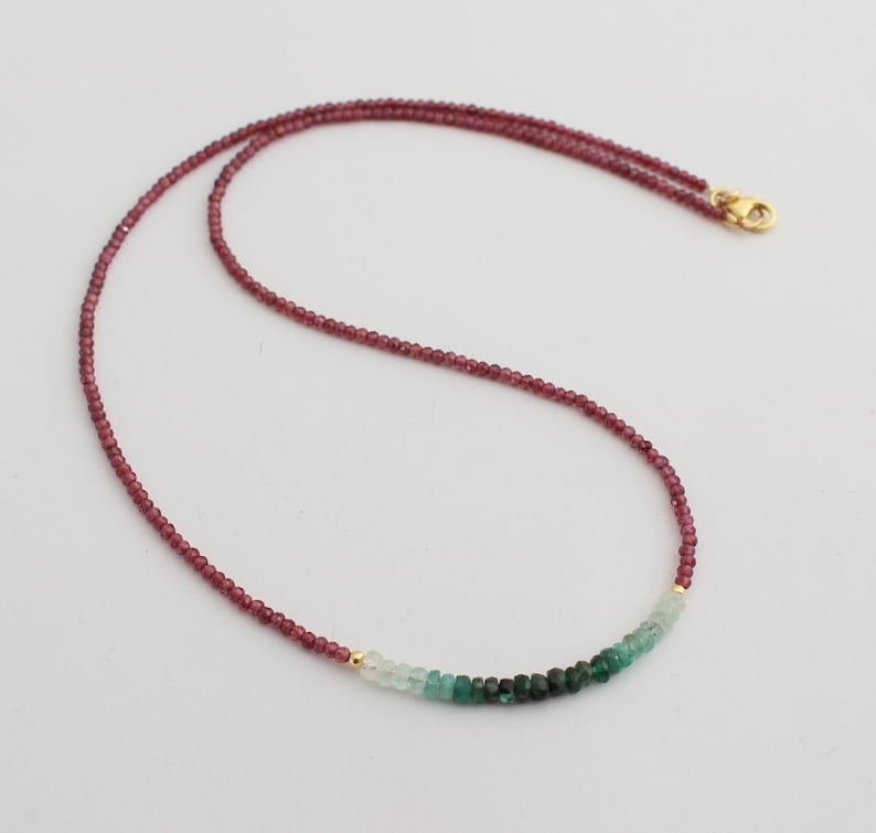 May include: A delicate gold chain necklace with a gradient of green and pink gemstones. The necklace features small, round beads in shades of pink, transitioning to light green and then dark green.