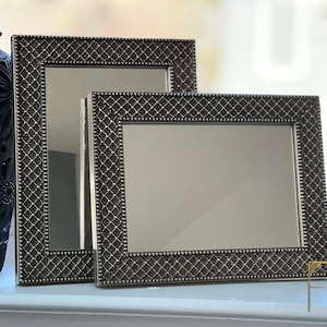 May include: Two silver-toned picture frames with a diamond pattern on the frame. The frames are nested inside each other, with the larger frame in the back and the smaller frame in the front.