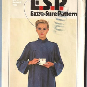 May include: A Simplicity 9219 sewing pattern envelope for a miss size K dress. The cover features a person wearing a long-sleeved, dark blue, high-neck dress while holding a white teacup and saucer. The text reads Simplicity 9219 E.S.P Extra-Sure Pattern.