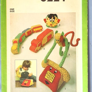 May include: Simplicity 8224 sewing pattern envelope featuring illustrations of fabric toys: a telephone, a clock face, a monkey, a truck, and a train. The pattern includes instructions for these stuffed items and a blue transfer for embroidery.