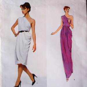 May include: Vogue Paris Original 2307 sewing pattern envelope featuring two one-shoulder dress designs. View A shows a knee-length white dress with a black belt. View B shows a floor-length purple dress with a thin belt. Both dresses feature draped fabric.