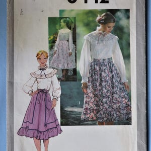 May include: A Simplicity 8442 sewing pattern envelope featuring illustrations and photographs of a blouse with a ruffled collar and long sleeves paired with a gathered skirt with a ruffled hem. The pattern displays a solid purple skirt and a floral skirt.