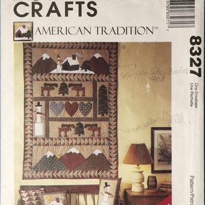 May include: McCall's Crafts 8327 American Tradition sewing pattern envelope featuring a quilt and pillow designs with mountains, moose, hearts, and snowmen. The cover displays a wall hanging, two square pillows, and one rectangular pillow.
