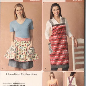 May include: Simplicity sewing pattern 2162 for one size aprons. The envelope displays various apron styles including a reversible version with a teapot print and a pull-over design with a spoon pattern, featuring pockets and trim details.