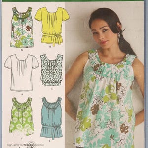 May include: Simplicity sewing pattern 2892 featuring six blouse designs. The pattern includes illustrations of blouses with various necklines, sleeves, and details. The image also shows a woman wearing a floral print blouse. Sizes H5 6,8,10,12,14.