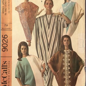 May include: A McCall's 9026 sewing pattern envelope featuring five variations of a loose-fitting tunic dress. The designs include a red patterned kaftan, a black and white striped dress, a color-blocked teal and white dress, and a brown dress with white trim.